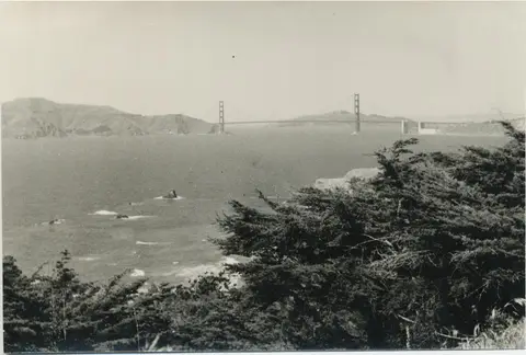 "Golden Gate Bridge." (Alkuperäinen kuvateksti.) Maisemaa merelle korkealta kuvattuna. Golden Gate Bridgen pylväät nousevat korkealle yli rantojen.