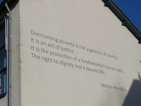 Afbeelding van een tekst van Nelson Mandela (1918-2013), geschilderd op de zijgevel van de Emmaus Kringloopwinkel Lombok (Makassarstraat 36) te Utrecht, aan de Keulsekade.N.B. De tekst luidt: "Overcoming poverty is not a gesture of charity. / It is an act of justice. / It is the protection of a fundamental human right, / The right to dignity and a decent life."